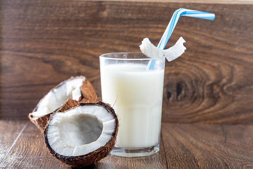 a glass of coconut milk with coconut halves on a brown table