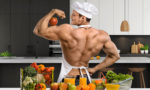 Muscular vegetarian guy in kitchen with veggies and fruit
